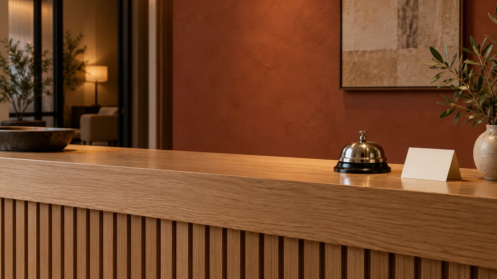 A quiet wooden reception counter with a metal service bell and an unprinted folded card